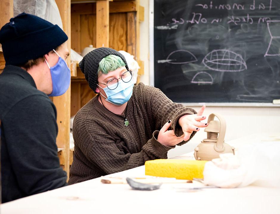 Student in a ceramics classroom talking to faculty.